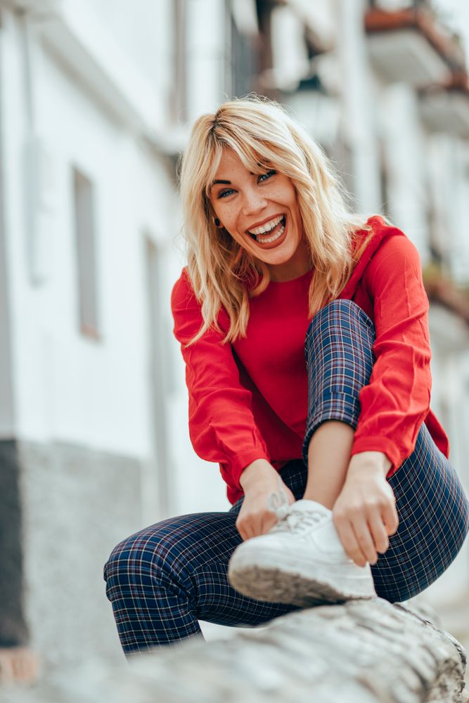 Laughing blonde female with red shirt sitting outside, vertical