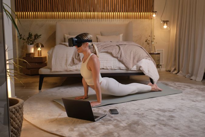 Woman in sportswear and VR goggles practicing yoga in Cobra pose