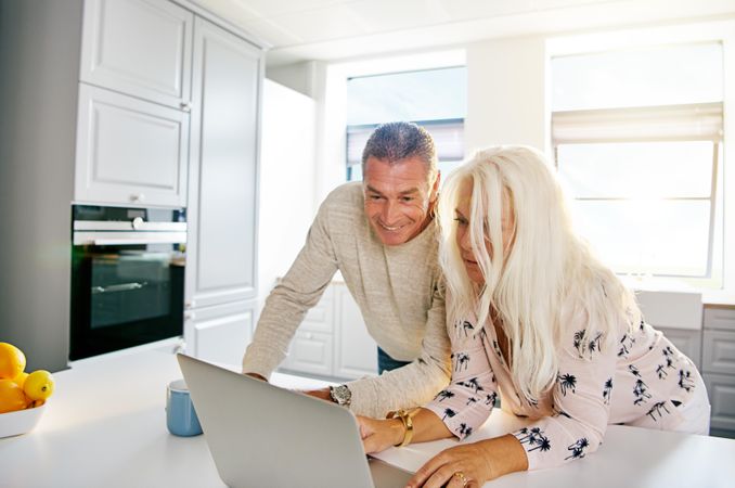Older couple in kitchen focused on their laptop
