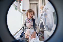 Upset boy with dirty clothes sitting near washing machine