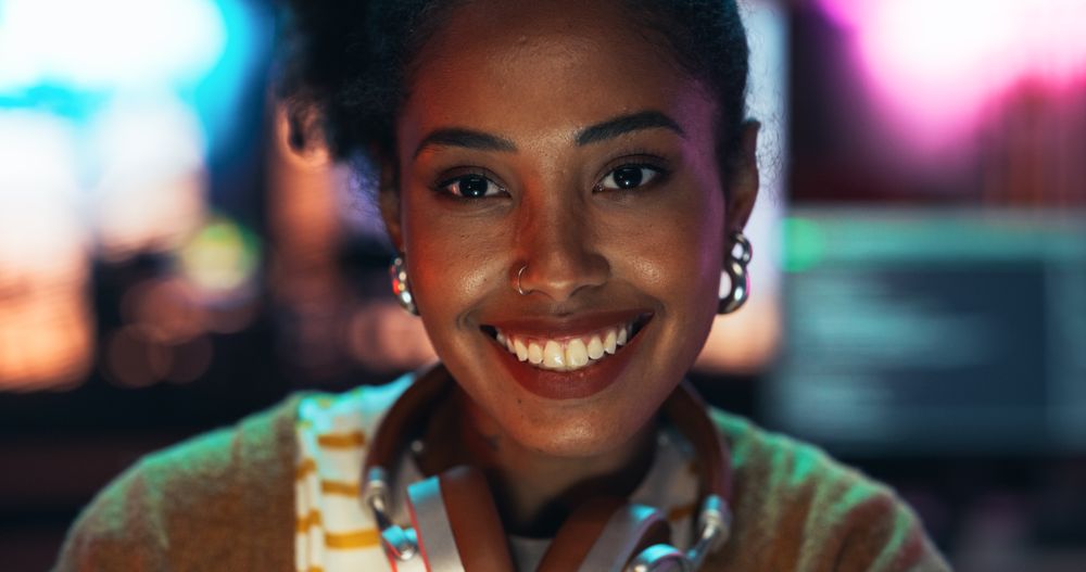 Portrait of a Stylish Young Black Woman with Headphones, Looking at Camera, and Smiling in a Creative Office.