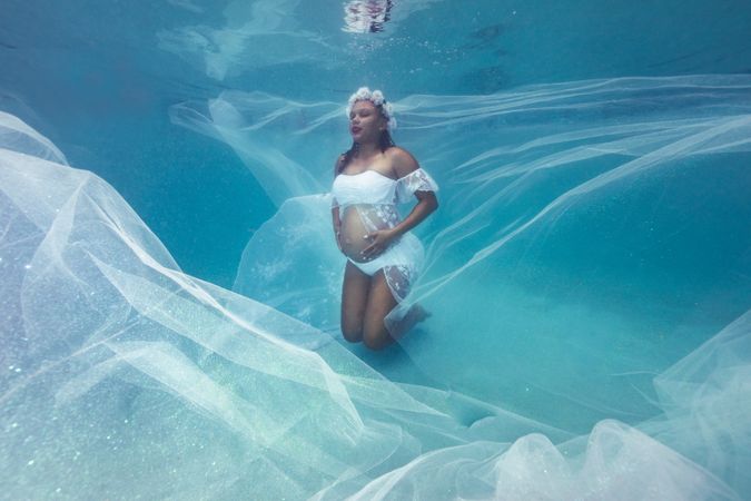 Pregnant woman in wreath and dress underwater