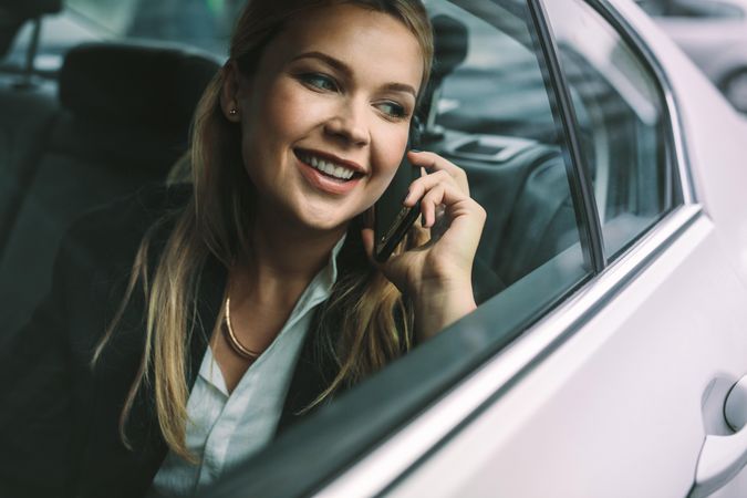 Smiling young businesswoman talking on the cell phone while sitting in back seat of a cab
