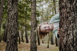 Smiling girl behind tree in forest