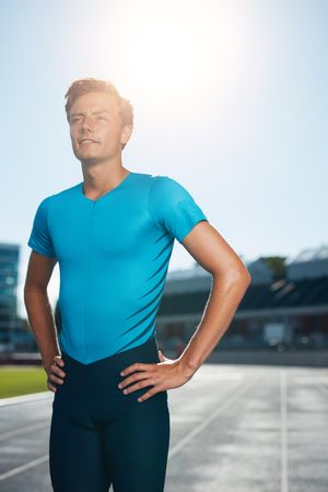 Young man athlete standing with his hands on hips staring into distance