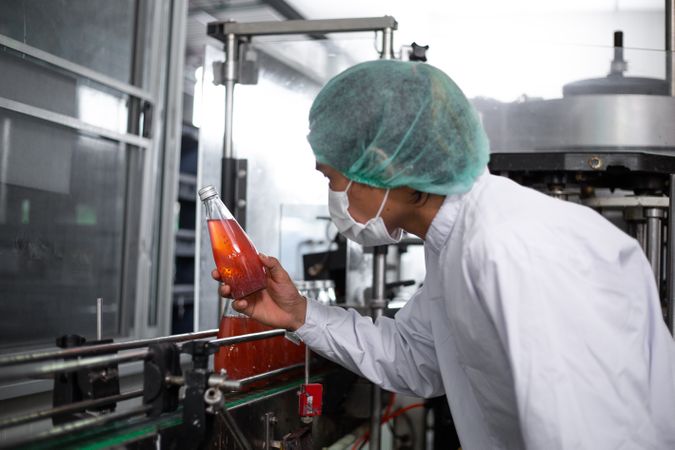 Asian man worker inspecting drink product on bottling factory machinery.