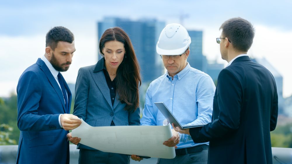 Team of Investors, Developers and Engineers Discuss Future of the Major Real Estate Project  with Major Contractor while Consulting Drafts and Plans.