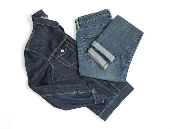 Folded denim jacket and jeans on light background