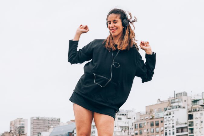 Content young woman in casual wear dancing while using headphones at city street
