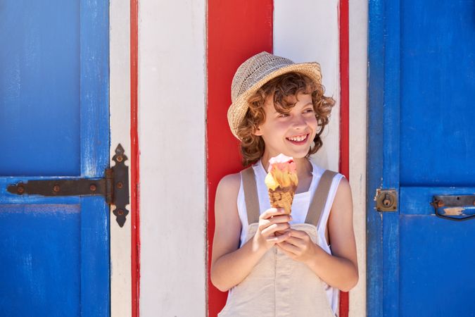 Cheerful boy in straw hat with ice cream near blue door