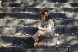 Child sitting on cement steps in outdoor park looking at a autumn leaf