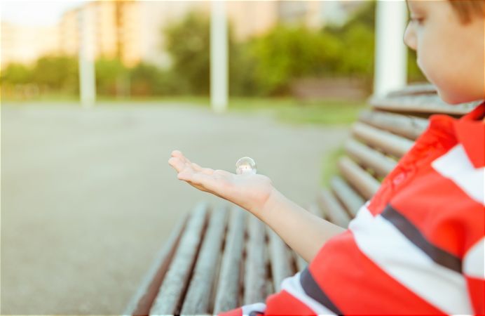 Cute boy looking soap bubble in his open hand