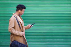 Side view of Cuban male texting on his phone in front of green wall