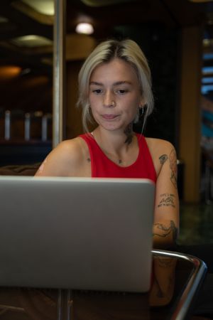 Young woman in red tank top typing on computer keyboard in a coffee shop