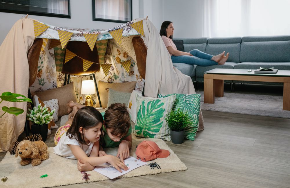 Children playing camping at home while their mother watches TV