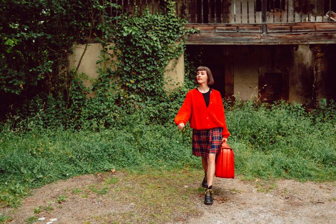 Woman in red with big red suitcase in forest