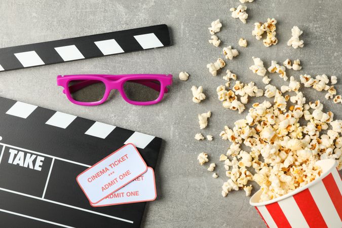 Clapperboard, tickets, 3d glasses and bucket with popcorn on grey background, top view