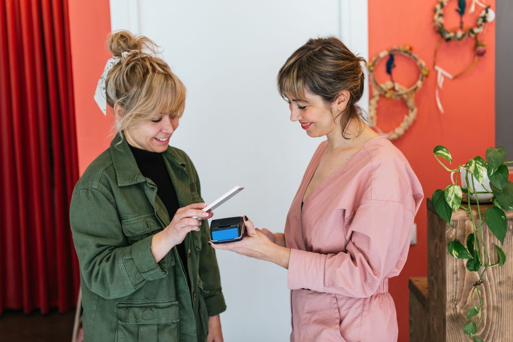 Delighted woman paying for skin care treatment with smartphone on POS terminal