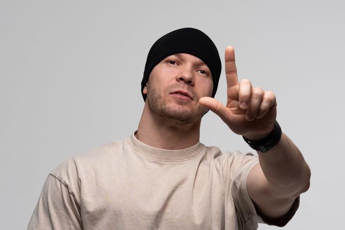 Man in beanie and beige t-shirt pointing forward