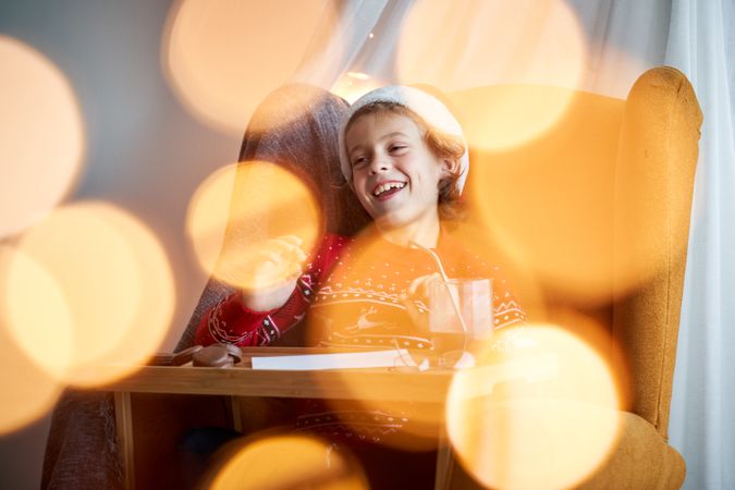 Joyful boy in Santa hat writing on paper