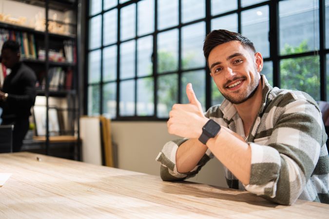 Man in bright office sitting at table giving thumbs up