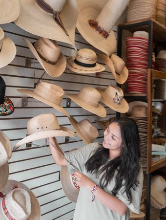 A young Hispanic woman is choosing a hat in a shop