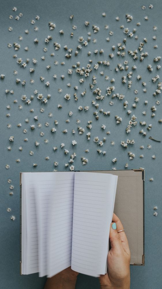 Person flipping blank notebook on blue background with tiny flowers around