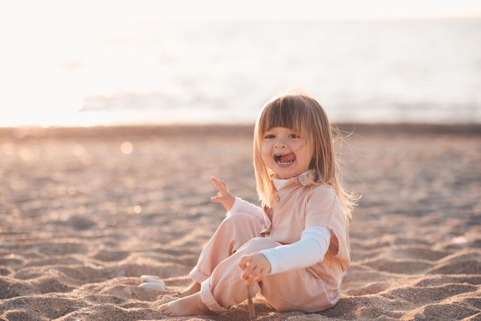 Girl making funny faces sitting on sandy seashore