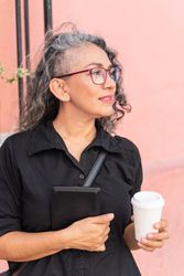 Fashionable woman in glasses holds tablet outdoors.