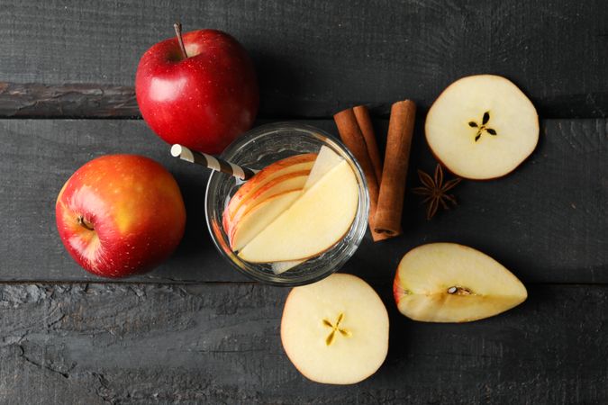 Top view of glass of water with straw, apple slices and cinnamon slices