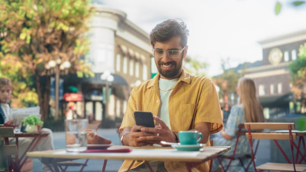 Handsome Indian Man Sitting on a Terrace in a Cafe, Having a Cup of Coffee with Pastry.