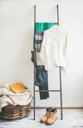 Woolen sweaters, jeans, grey scarf, winter boots on modern garment rack, with thatched basket