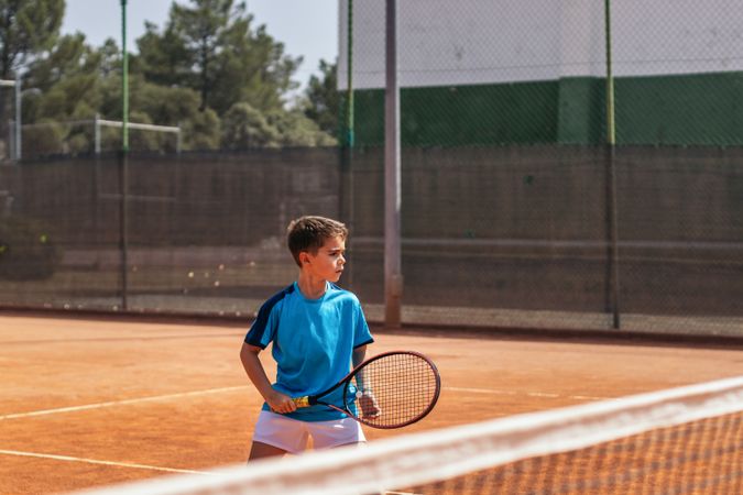 Little boy playing tennis on a dirt court