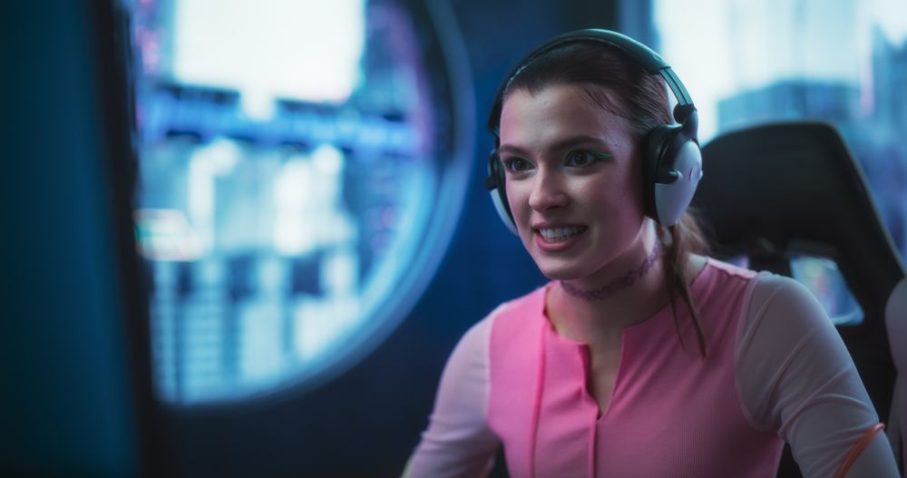 Portrait of a Young Female Wearing Headphones, Talking on a Video Call with Friends while Playing Video Games Online on a Computer.
