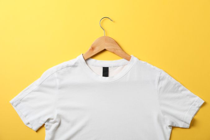 Hanger with blank plain t-shirt on yellow background, space for text