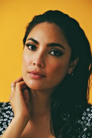 Headshot of Hispanic woman looking at camera in yellow tilting her head, vertical