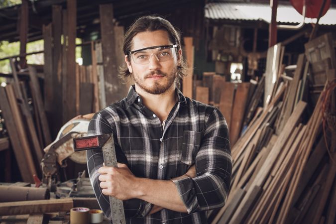 Portrait of male carpenter wearing protective glasses and holding woodworking tool in workshop