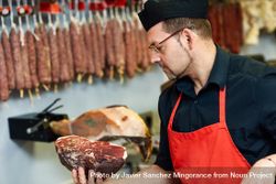 Man in butcher shop holding cut meat 0gKYj0