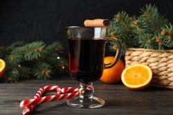 Glass of tasty mulled wine on decorated wooden background, space for text