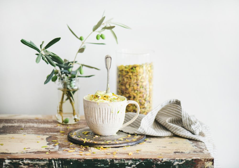 Cup of pistachio ice cream with spoon, on wooden table with leaves, and table linen