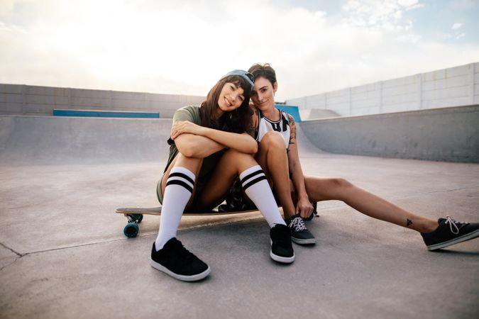 Two female skateboarders sitting on a long board at skate park