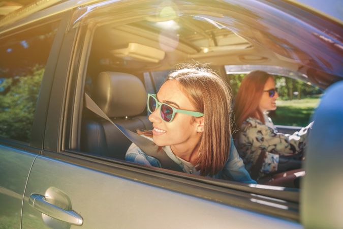 Happy young woman looking back through passenger window in car