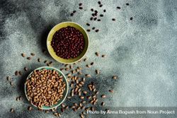 Top view of bowls of dried legumes from pantry on grey table with copy space 0PjvZO