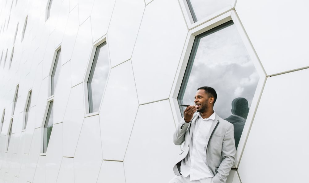 Elegant Black man talking smartphone leaning on geometrical wall