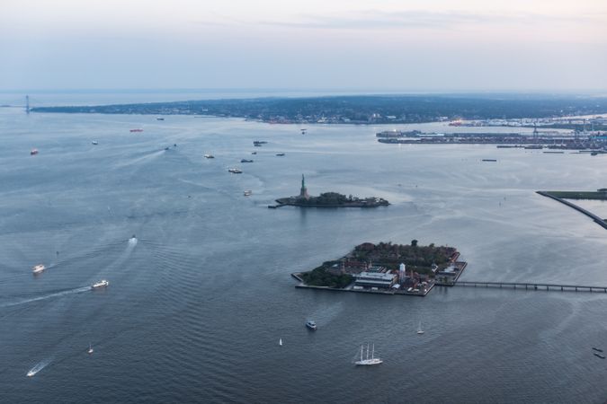 Aerial Helicopter Cinematic Passing View of the Statue of Liberty with Manhattan Skyline Cityscape. Panoramic View of New York City Skyscrapers and Jersey City Buildings on a Cloudy Afternoon