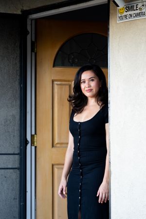 Woman in dark dress smiling and looking at camera in front of her home
