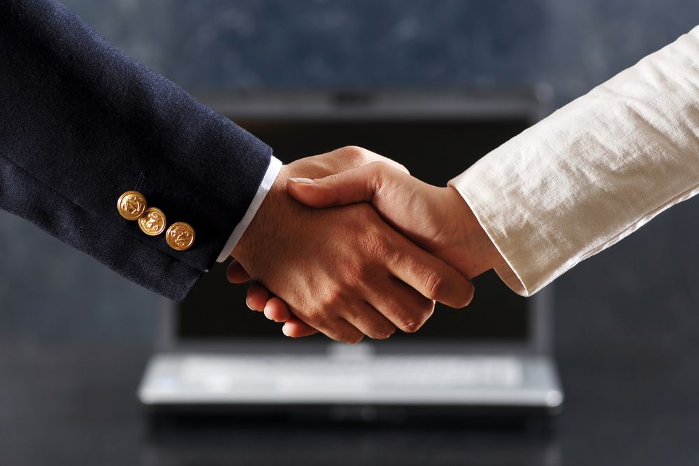Professional Business Handshake Between Two People with a Laptop Background
