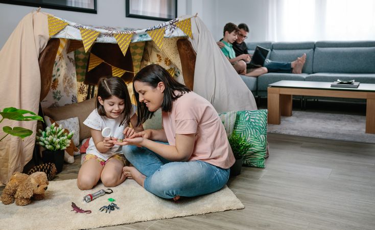 Mother and daughter playing while father and son use laptop