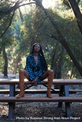 Fashion photo of woman in blue flannel shirt and tall boots sitting on bench in the mountains 0yXwab