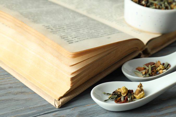 Book and herbs in scoops on wooden background, close up